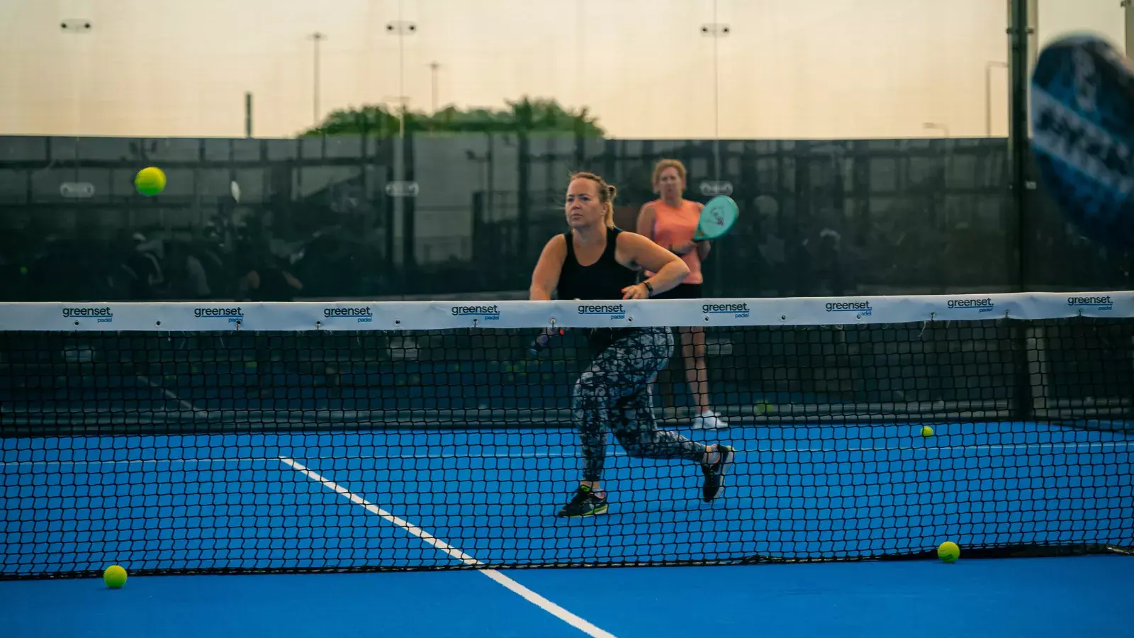 Woman running after a ball with her racket raised during a Padel game.